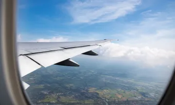 An airplane window overlooking the wingtip and ground below 